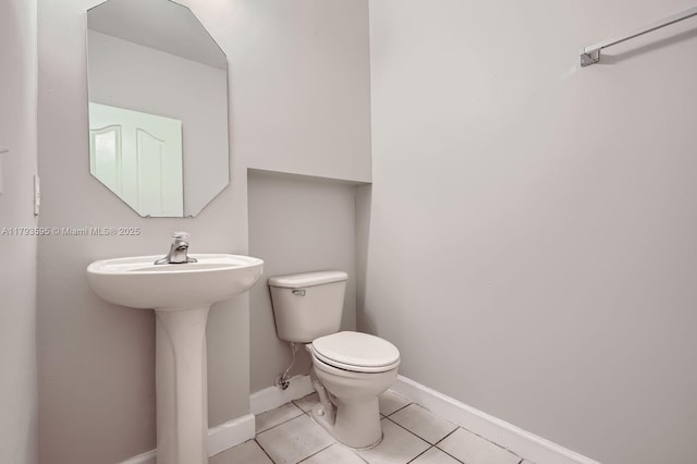 half bath with toilet, baseboards, and tile patterned flooring