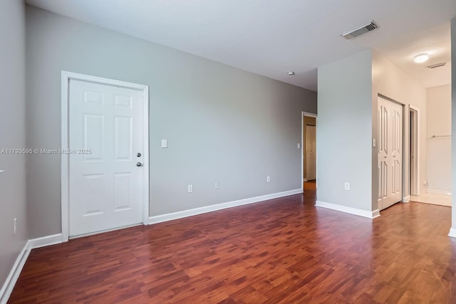 unfurnished room with baseboards, visible vents, and dark wood-type flooring
