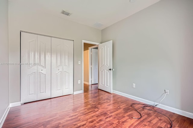 unfurnished bedroom featuring baseboards, a closet, wood finished floors, and visible vents