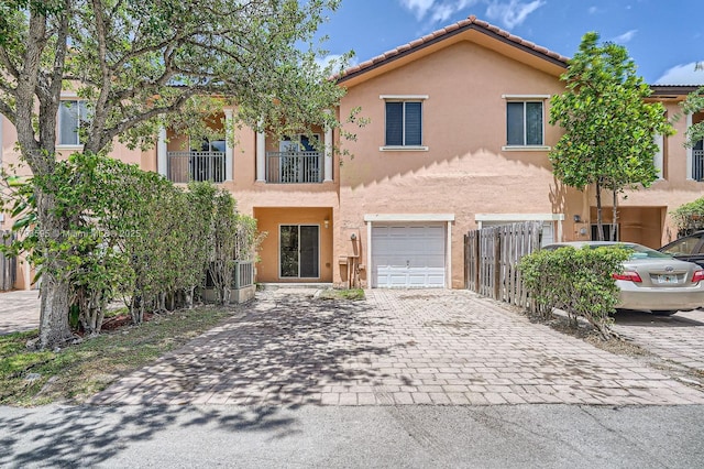 view of front of home featuring fence, decorative driveway, stucco siding, a tiled roof, and an attached garage