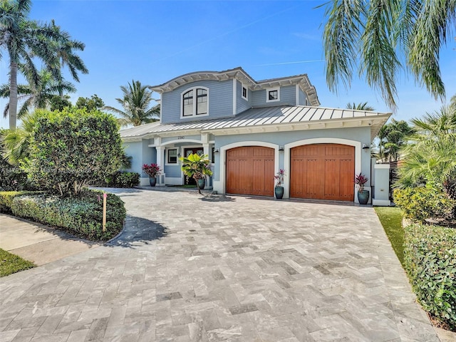 mediterranean / spanish-style home with a garage, decorative driveway, stucco siding, a standing seam roof, and metal roof