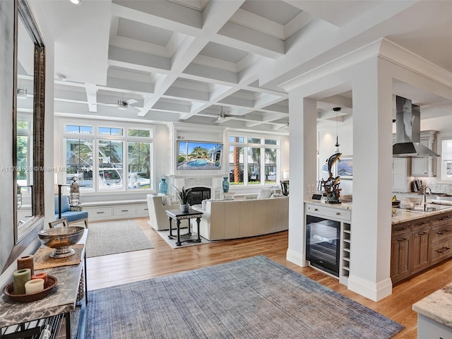 living area featuring a fireplace, beamed ceiling, beverage cooler, ceiling fan, and coffered ceiling