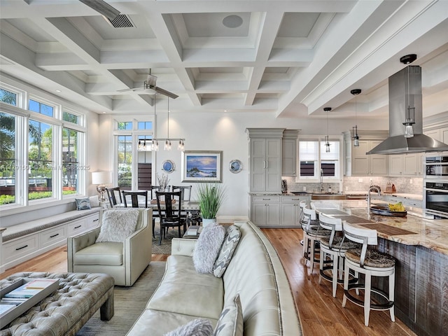 living area featuring a ceiling fan, visible vents, beam ceiling, light wood finished floors, and coffered ceiling