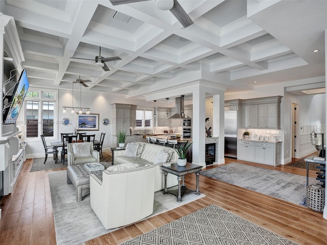 living area with a ceiling fan, wine cooler, beam ceiling, and light wood-type flooring