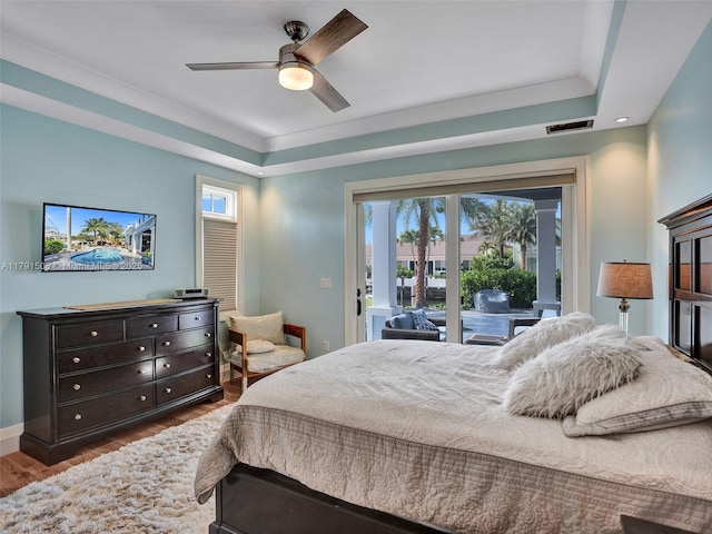 bedroom featuring access to outside, dark wood finished floors, baseboards, a tray ceiling, and visible vents