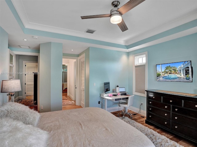 bedroom featuring visible vents, wood finished floors, baseboards, a tray ceiling, and recessed lighting