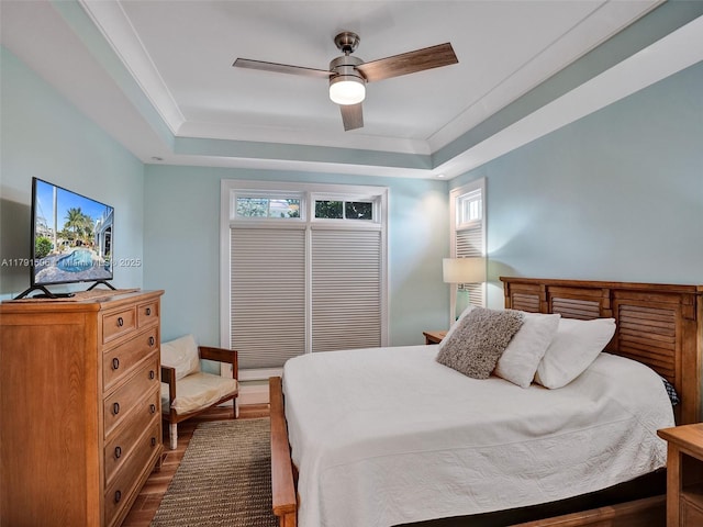 bedroom featuring a ceiling fan, a tray ceiling, and dark wood-type flooring