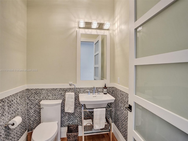half bath with toilet, tile walls, and a wainscoted wall