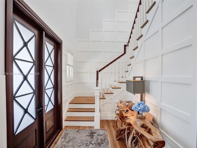 entryway featuring french doors, wood finished floors, stairway, and a decorative wall