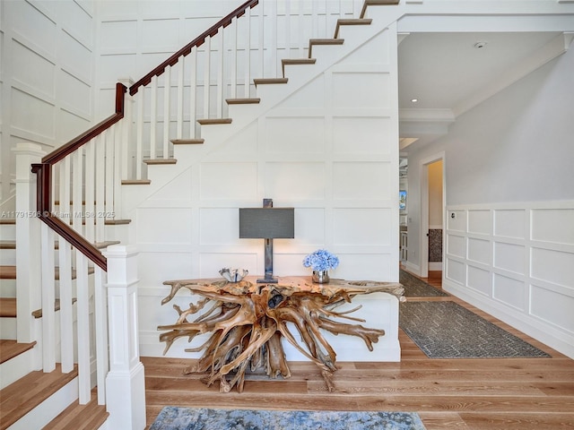 staircase featuring crown molding, wood finished floors, and a decorative wall