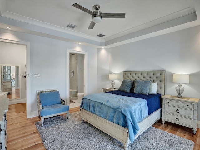 bedroom with a tray ceiling, visible vents, and wood finished floors
