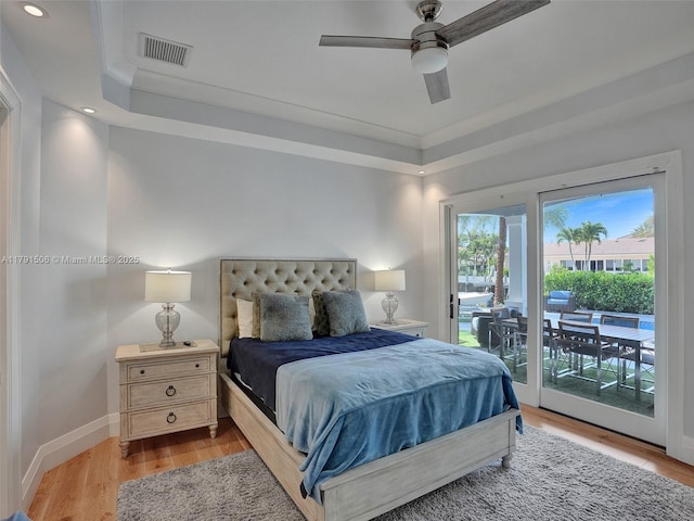bedroom featuring access to outside, light wood finished floors, a tray ceiling, and visible vents