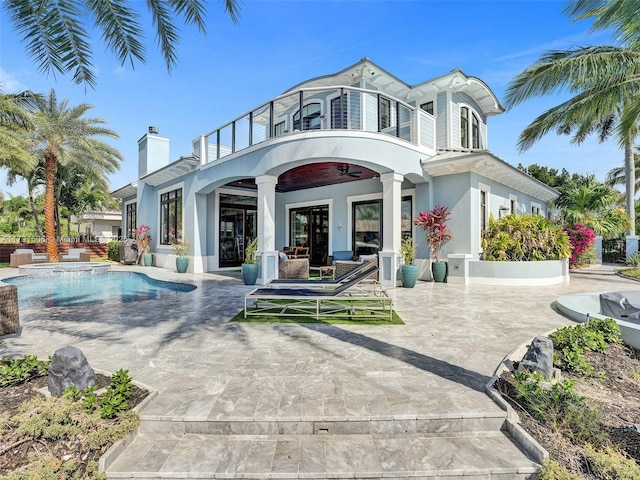 back of property with stucco siding, an outdoor pool, a chimney, a patio area, and a balcony