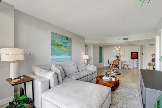 living area with visible vents, baseboards, wood finished floors, and an inviting chandelier