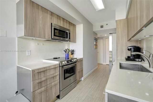 kitchen with light brown cabinetry, modern cabinets, a sink, light countertops, and stainless steel appliances