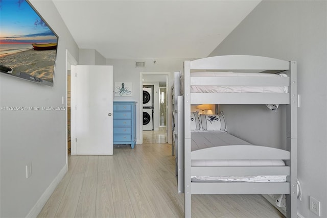 bedroom featuring baseboards, stacked washer / drying machine, visible vents, and wood finished floors