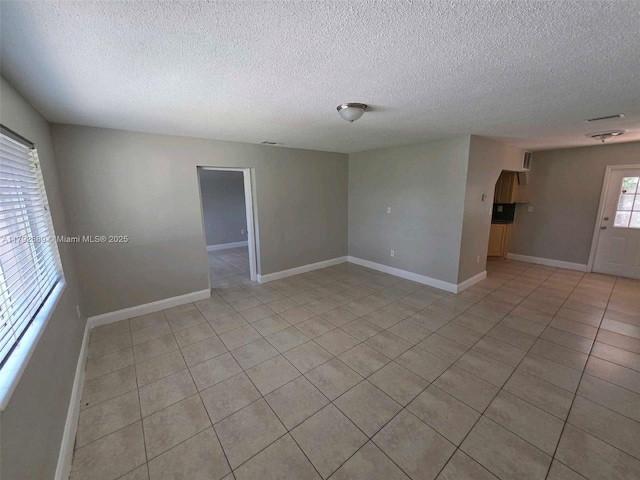 empty room with baseboards, a textured ceiling, and light tile patterned floors
