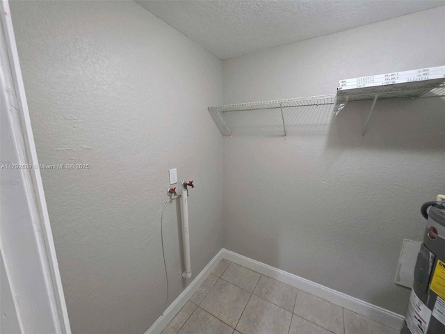laundry area with laundry area, a textured ceiling, baseboards, light tile patterned floors, and electric water heater