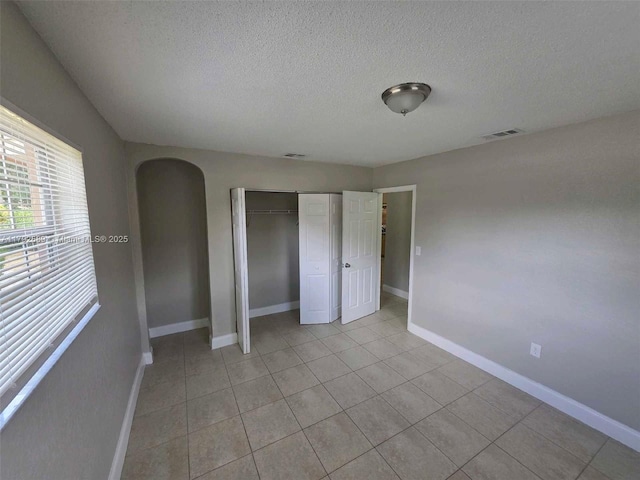 unfurnished bedroom with arched walkways, a textured ceiling, baseboards, light tile patterned floors, and visible vents