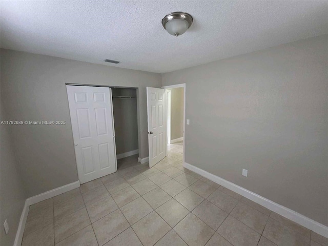 unfurnished bedroom with baseboards, a textured ceiling, light tile patterned flooring, and a closet