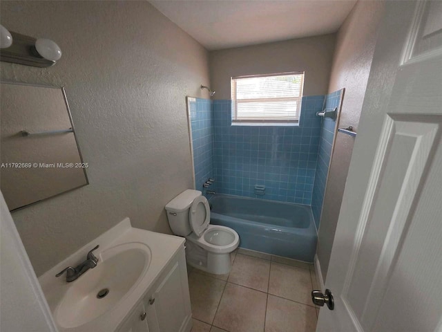 full bathroom with tile patterned floors, vanity, toilet,  shower combination, and a textured wall