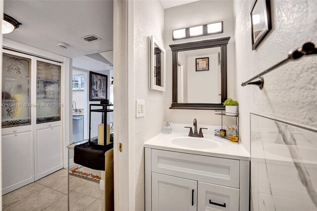 bathroom with vanity, tile patterned flooring, a textured wall, and visible vents
