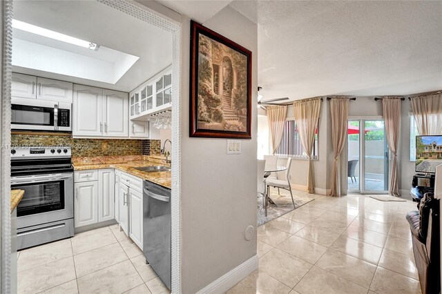 kitchen featuring decorative backsplash, appliances with stainless steel finishes, a sink, baseboards, and white cabinetry