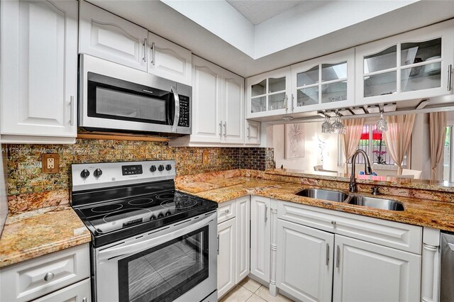kitchen featuring tasteful backsplash, a sink, white cabinets, glass insert cabinets, and stainless steel appliances