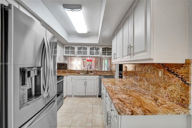 kitchen featuring tasteful backsplash, a sink, glass insert cabinets, stainless steel appliances, and white cabinetry