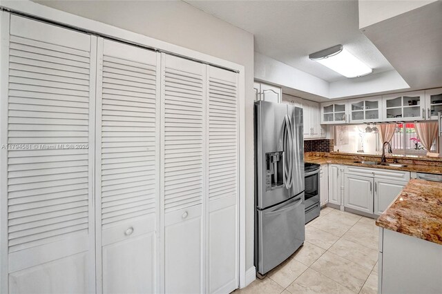 kitchen featuring decorative backsplash, a sink, light tile patterned floors, glass insert cabinets, and stainless steel appliances