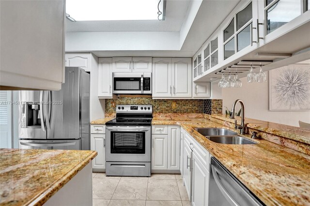 kitchen with light stone countertops, a sink, stainless steel appliances, backsplash, and glass insert cabinets