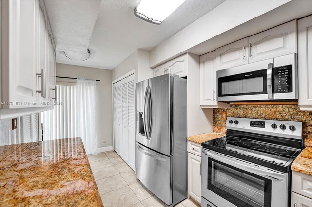 kitchen featuring appliances with stainless steel finishes, tasteful backsplash, white cabinetry, baseboards, and light tile patterned flooring