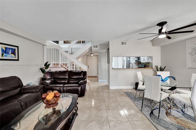 living room featuring visible vents, a ceiling fan, stairs, and baseboards