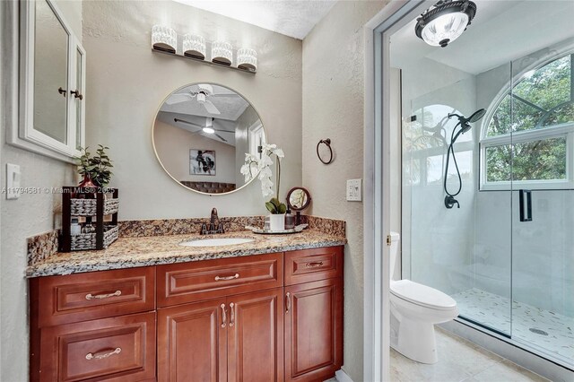 bathroom with a ceiling fan, a shower stall, vanity, toilet, and a textured wall