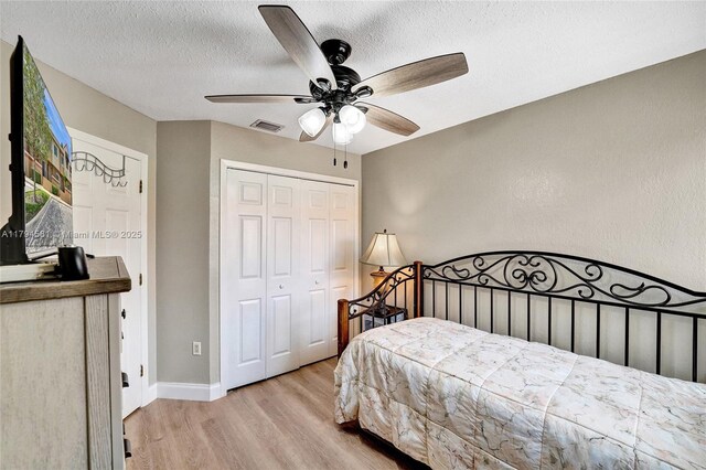 bedroom with a textured ceiling, a ceiling fan, wood finished floors, visible vents, and a closet