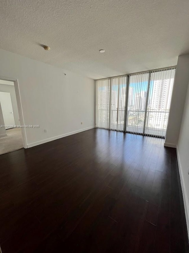 empty room featuring dark wood-type flooring, a textured ceiling, and baseboards