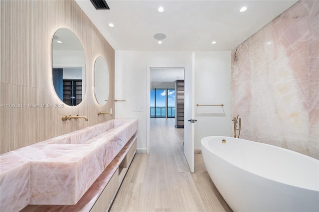 bathroom with visible vents, wood finished floors, vanity, a soaking tub, and recessed lighting