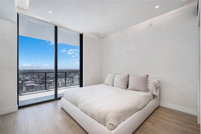 bedroom with access to outside, baseboards, expansive windows, and wood finished floors