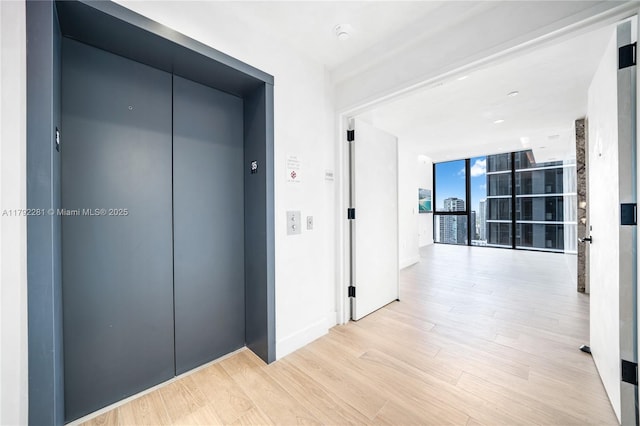 corridor with baseboards, floor to ceiling windows, elevator, and light wood-style flooring
