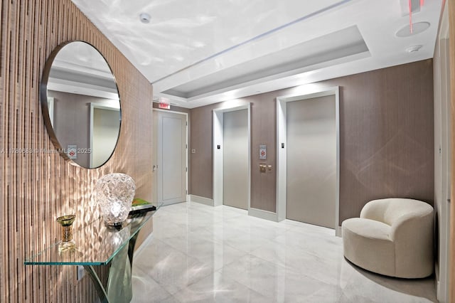 corridor featuring a tray ceiling, elevator, and marble finish floor