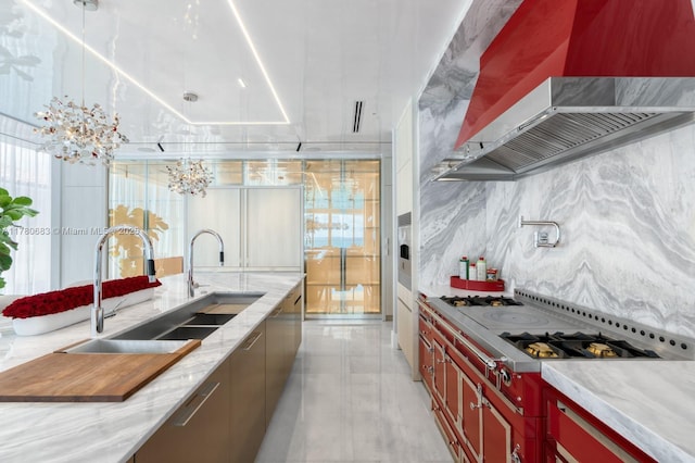 kitchen featuring stovetop with downdraft, backsplash, light stone countertops, a sink, and wall chimney exhaust hood