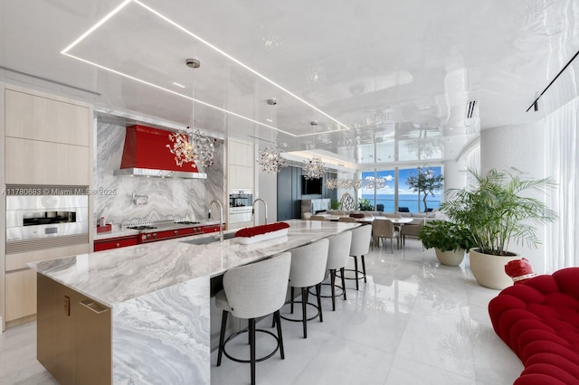 kitchen with light stone countertops, stainless steel appliances, a large island with sink, custom exhaust hood, and modern cabinets