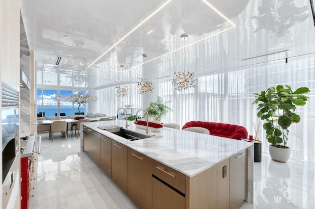kitchen with modern cabinets, light stone countertops, a spacious island, a sink, and open floor plan