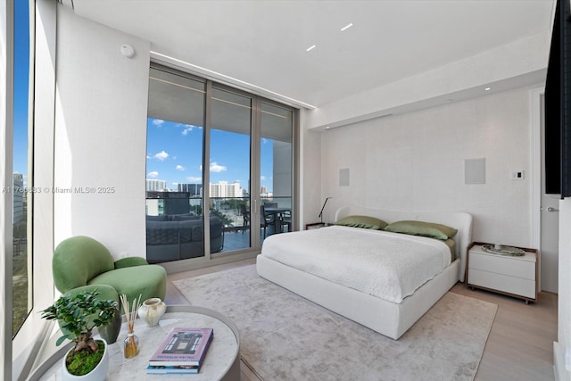 bedroom featuring a view of city, a wall of windows, access to exterior, and light wood finished floors