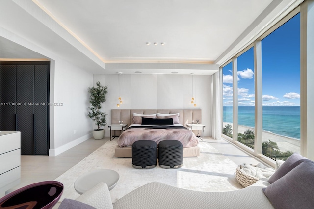 bedroom featuring wood finished floors, expansive windows, baseboards, a water view, and access to outside