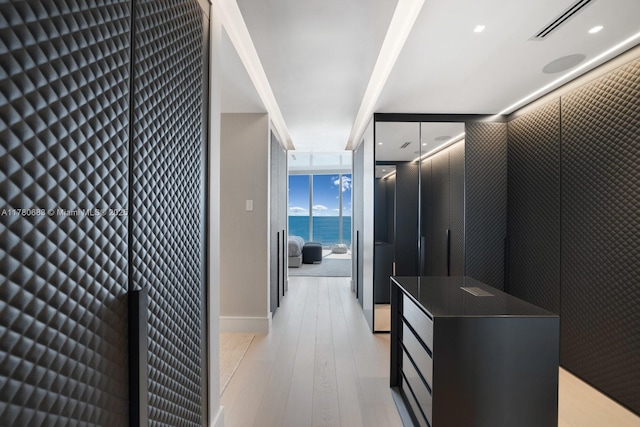 hall with visible vents, a heating unit, light wood-style flooring, baseboards, and floor to ceiling windows