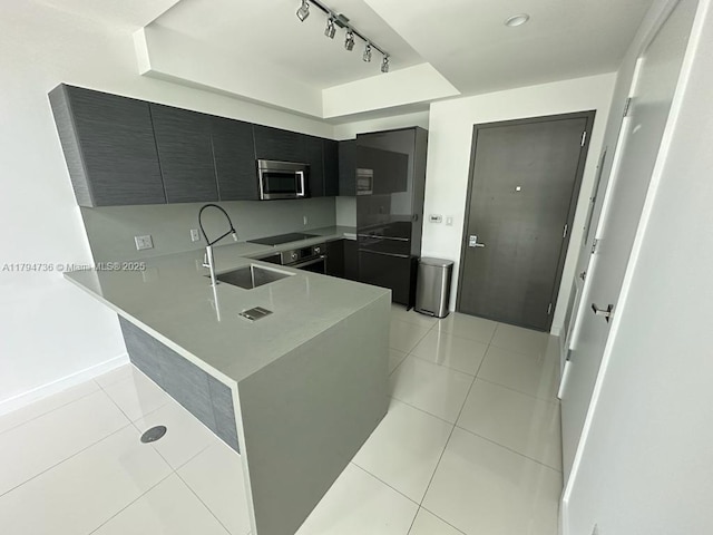 kitchen featuring track lighting, a sink, dark cabinetry, stainless steel microwave, and light tile patterned floors