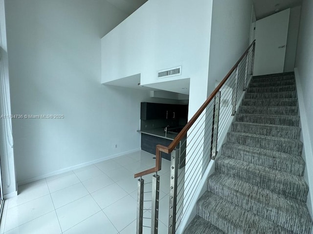 stairs with baseboards, a high ceiling, tile patterned floors, and visible vents
