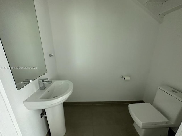 half bathroom with toilet, baseboards, and tile patterned floors
