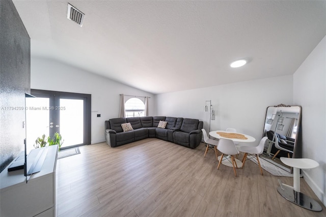living area with visible vents, lofted ceiling, french doors, and light wood-type flooring